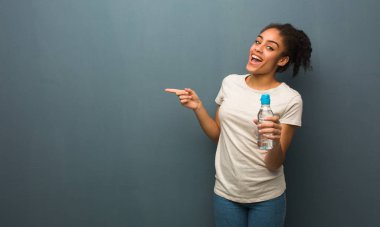 Genç siyahi kadın parmağıyla kenarı işaret ediyor. Elinde bir su şişesi var..