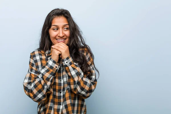 Young cool indian woman keeps hands under chin, is looking happily aside.