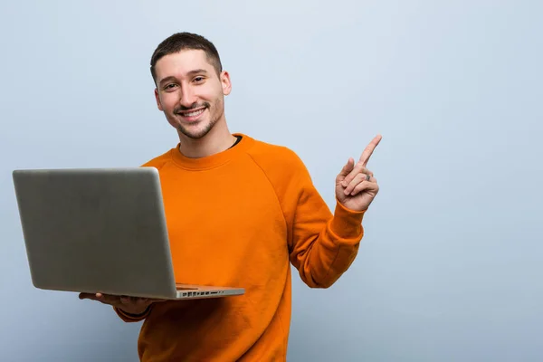 Jovem Caucasiano Segurando Laptop Sorrindo Alegremente Apontando Com Dedo Indicador — Fotografia de Stock