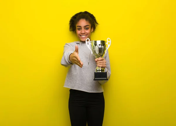 Young fitness black woman reaching out to greet someone. Holding a trophy.