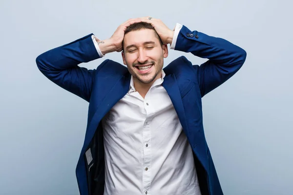 Young business caucasian man laughs joyfully keeping hands on head. Happiness concept.