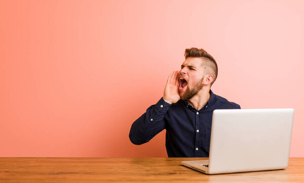 Молодой человек, работающий с ноутбуком, крича и держа ладонь у открытого рта
.