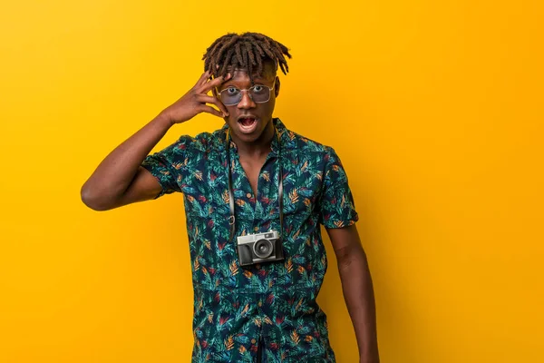 Young black rasta man wearing a vacation look blink at the camera through fingers, embarrassed covering face.