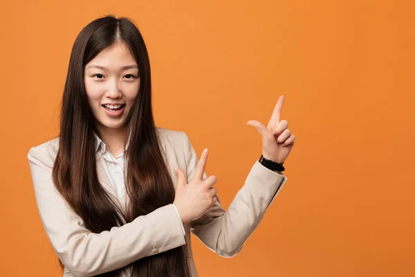 Young business chinese woman pointing with forefingers to a copy space, expressing excitement and desire.