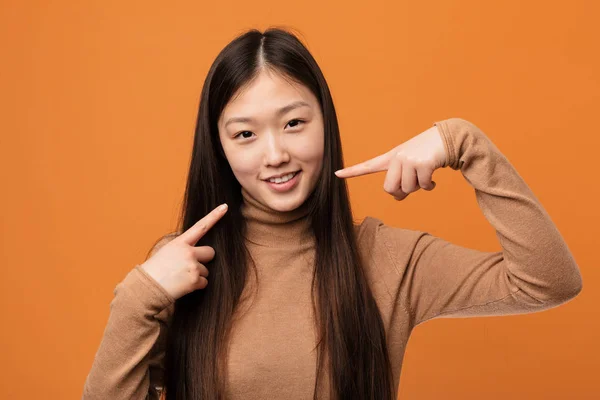 Young pretty chinese woman smiles, pointing fingers at mouth.