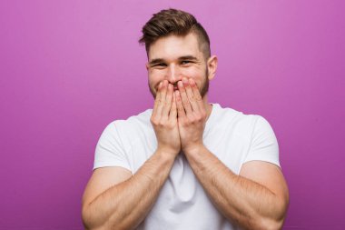 Genç yakışıklı beyaz adam bir şey hakkında gülüyor, elleriyle ağız kapsayan.