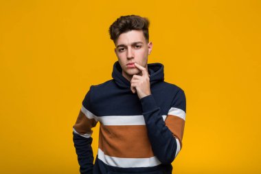 Kapüşonlu bir genç adam şüpheli ve şüpheci bir ifadeyle yana bakıyor..