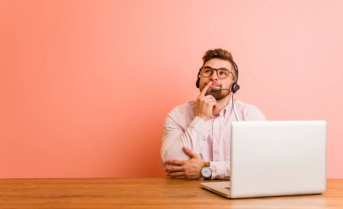 Bir çağrı merkezinde çalışan genç adam şüpheli ve şüpheci ifade ile yana bakıyor.