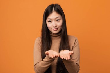 Genç, güzel Çinli bir kadın avuçlarıyla bir şey tutuyor ve kameraya sunuyor..