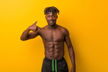 Genç siyahi, üstsüz, mayosuz bir adam gömleğin fotokopi odasını elle gösteriyor, gururlu ve kendinden emin.