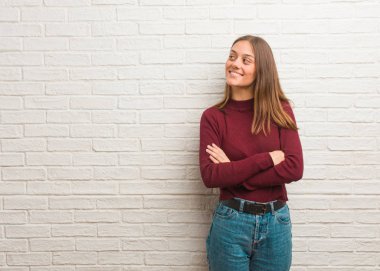 Tuğla duvarın üzerinden kendine güvenen ve kollarını kavuşturan genç, havalı bir kadın.