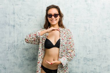 Bikini giyen genç Avrupalı kadın iki eliyle bir şey tutuyor, ürün sunumu..