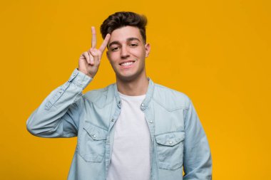 Kot gömlek giyen genç yakışıklı öğrenci zafer işareti gösteriyor ve gülümsüyor..