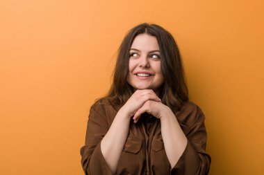 Genç kıvrımlı Rus kadın ellerini çenesinin altında tutuyor, mutlu bir şekilde yan tarafa bakıyor..