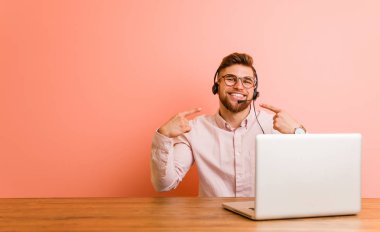 Çağrı merkezinde çalışan genç adam gülümsüyor, parmaklarını ağzına doğrultuyor..