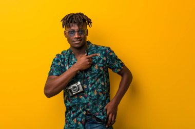 Tatil giymiş genç siyah Rasta adam gülümsüyor ve boş alanda bir şeyler gösteriyor..