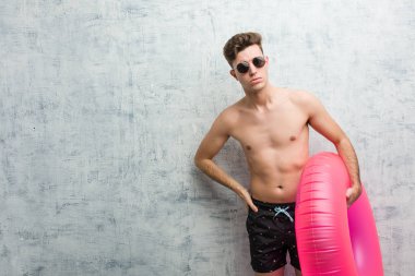 Elinde pembe şişme bir çörek tutan, mayo giyen genç bir adam çok kızgın birini azarlıyor..