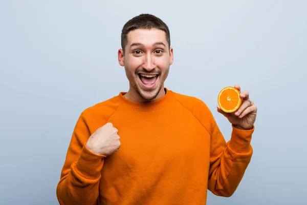 Νεαρός Καυκάσιος Που Κρατάει Ένα Πορτοκάλι Ξαφνιασμένος Δείχνοντας Τον Εαυτό — Φωτογραφία Αρχείου