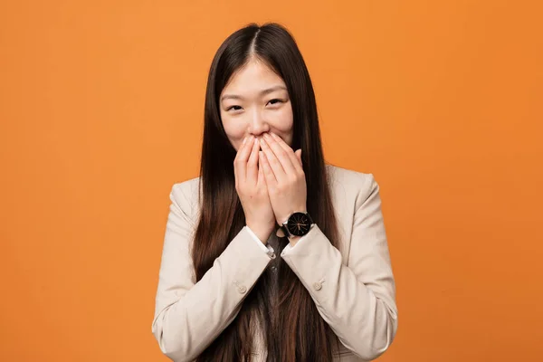 Young business chinese woman laughing about something, covering mouth with hands.