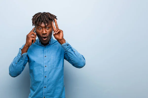 Young rasta black man holding a phone showing victory sign and smiling broadly.