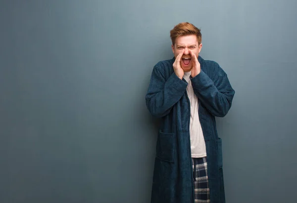 Young redhead man in pajama shouting something happy to the front