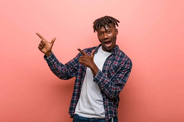 Young african black man pointing with forefingers to a copy space, expressing excitement and desire.