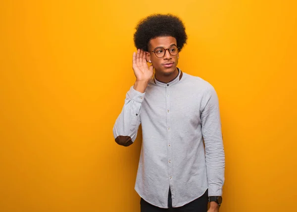 オレンジ色の壁の上に若いアフリカ系アメリカ人の男はゴシップを聞いてみる — ストック写真