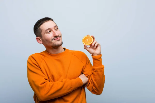 Joven Hombre Caucásico Sosteniendo Una Naranja Sonriente Confiado Con Los — Foto de Stock