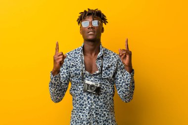 Tatil kıyafeti giyen siyah Rasta 'lı genç adam iki elini de havaya kaldırarak boş bir alan gösterdiğini gösteriyor..