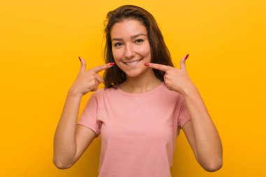 Genç Avrupalı kadın sarı arka plan üzerinde izole gülümsüyor, ağız da parmakları işaret.