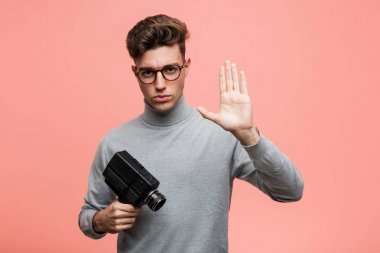 Genç entellektüel bir adam elinde bir film kamerasıyla elini uzatmış, dur işareti göstererek seni engelliyor..