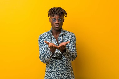 Genç siyah Rasta tatile çıkmış. Elinde avuç içi olan bir şeyle kameraya sunuyor..