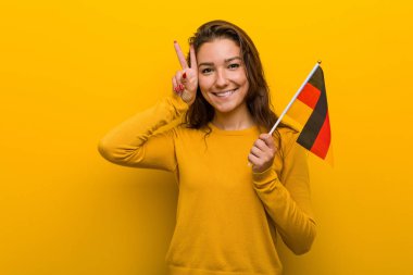 Genç Avrupalı kadın elinde bir Alman bayrağı, zafer işareti taşıyor ve gülümsüyor..