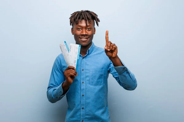 Young rasta black man holding an air tickets showing number one with finger.
