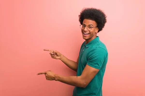 年轻的非洲裔美国人在粉红色的墙上用手指指着一边 — 图库照片