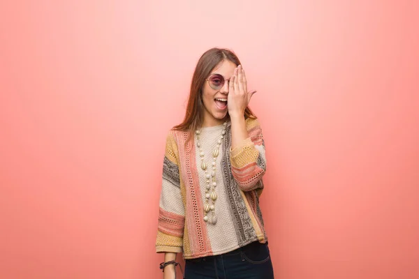 Young hippie woman on pink background shouting happy and covering face with hand