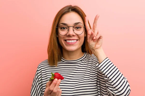Mujer Joven Sosteniendo Una Fresa Mostrando Signo Victoria Sonriendo Ampliamente —  Fotos de Stock