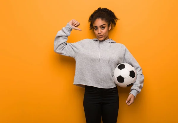 Young fitness black woman pointing fingers, example to follow. Holding a soccer ball.