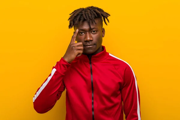 Young fitness african man pointing temple with finger, thinking, focused on a task.