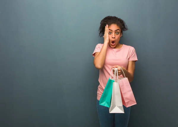 Young black woman surprised and shocked. She is holding a shopping bags.