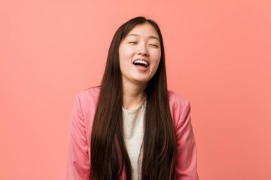 Pembe takım elbiseli genç Çinli kadın gevşemiş ve mutlu bir şekilde gülüyor, boynunu uzatmış dişlerini gösteriyor..