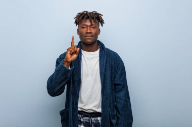 Genç Afrikalı siyah adam pijama giyiyor. Parmağıyla bir numarayı gösteriyor..