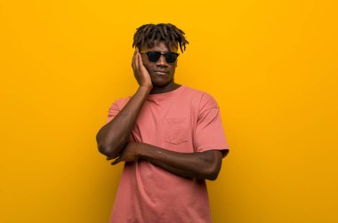 Güneş gözlüğü takan, sıkılmış, yorgun ve dinlenmeye ihtiyacı olan genç siyahi bir adam..