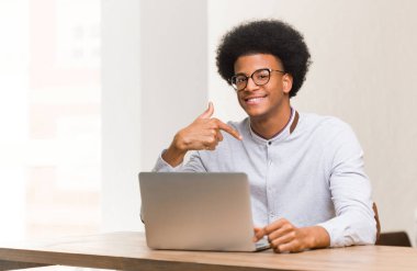 Genç siyahi adam dizüstü bilgisayarını kullanarak gömlek fotokopisini çekiyor.