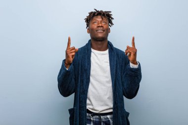 Pijama giyen Afrikalı genç bir adam iki parmağını da havaya kaldırarak boş bir alan gösteriyor..