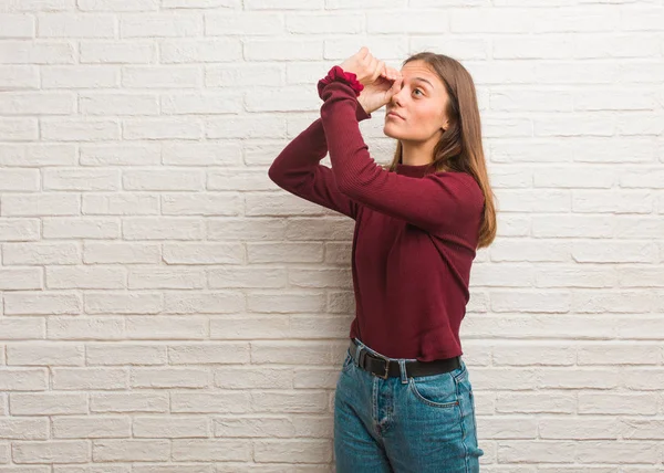 Young cool woman over a bricks wall making the gesture of a spyglass