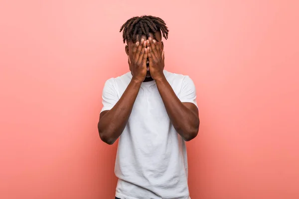 Young african black man covers eyes with hands, smiles broadly waiting for a surprise.