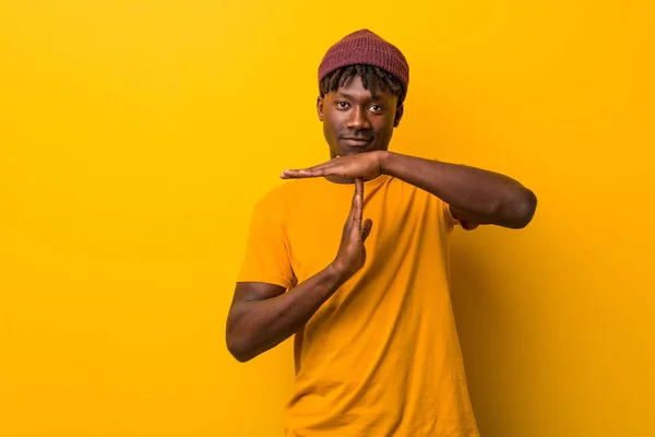 Young black man wearing rastas over yellow background showing a timeout gesture.