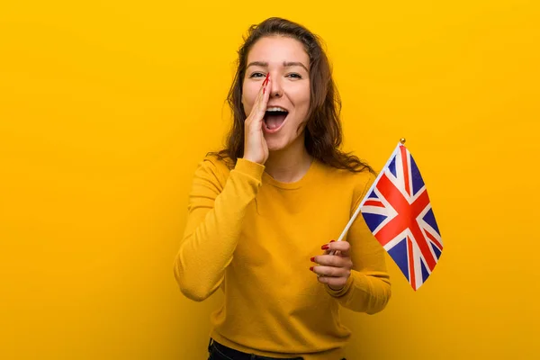 Young european woman holding an united kingdom flag shouting excited to front.