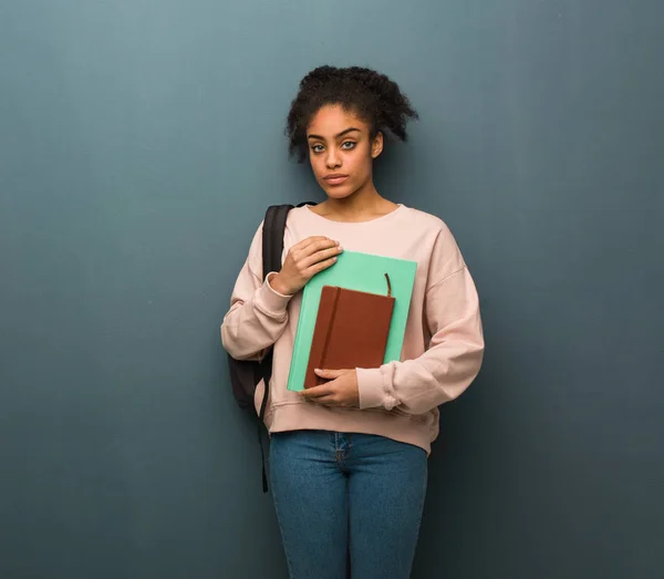 Young student black woman looking straight ahead. She is holding books.